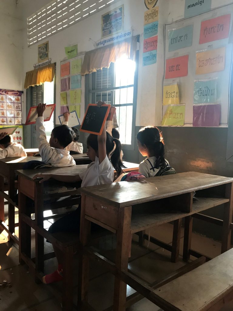 Kambodzalaiset lapset viittaavat luokassa pidelleen pieniä liitutauluja ylhäällä.