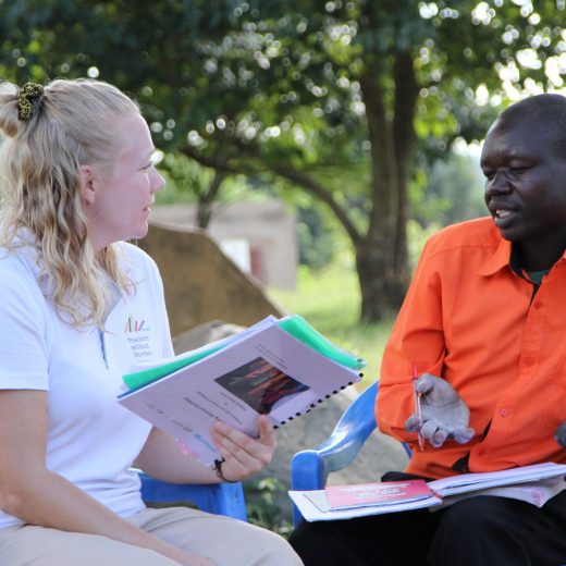 Suomalainen vapaaehtoinen kuuntelee ugandalaista opettajaa. Heillä on käsissään papereita.