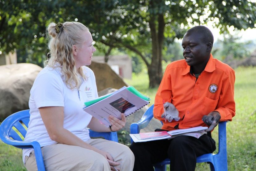 Suomalainen vapaaehtoinen istuu ugandalaista opettajaa vastapäätä ja kuuntelee häntä. Kummallakin on käsissään tai sylissään paperipino.