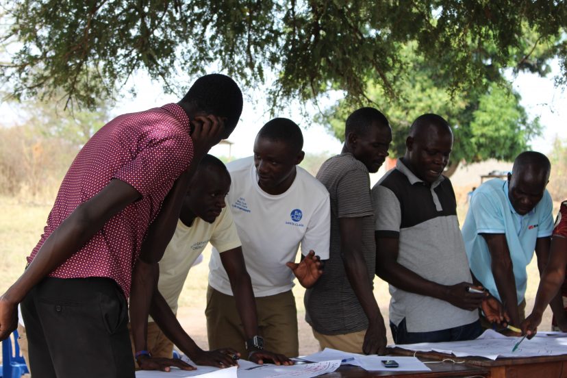 Joukko ugandalaisia miehiä keskustelee edessään iso paperi pöydällä.