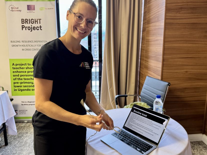 Nainen seisoo tietokoneen edessä ja tekee narulla solmua. A woman focuses on tying a knot with a string while standing at a desk with a laptop. The activity is part of a hands-on training session.