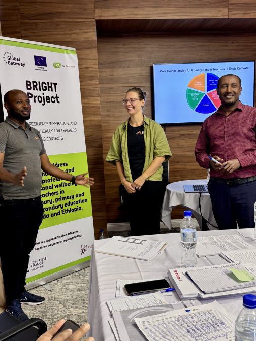 Kaksi miestä ja yksi nainen seisoo banderollin edessä ja hymyilee. Three people stand side by side, smiling at the camera. Behind them is a banner related to the TiCC training program.